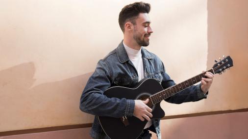 Imagem de um homem jovem em pé, tocando um violão