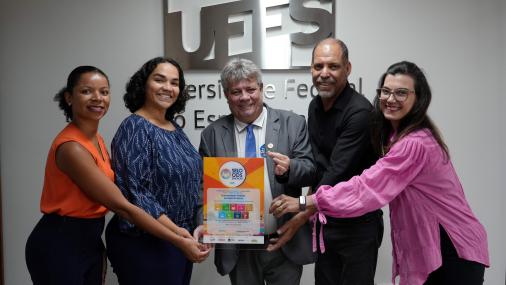 Foto do reitor segurando a placa que simboliza o selo, ao lado das servidoras técnicas administrativas e dos pró-reitores de Extensão e Gestão de Pessoas