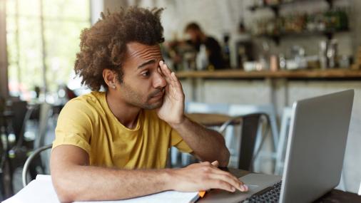 Jovem estudando diante de um notebook com a mão no rosto