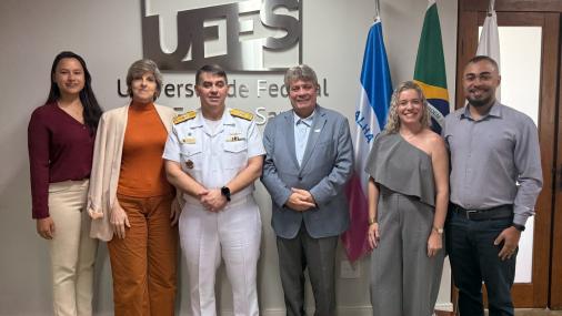 foto dos participantes da reunião em frente à parede com a logomarca da Ufes